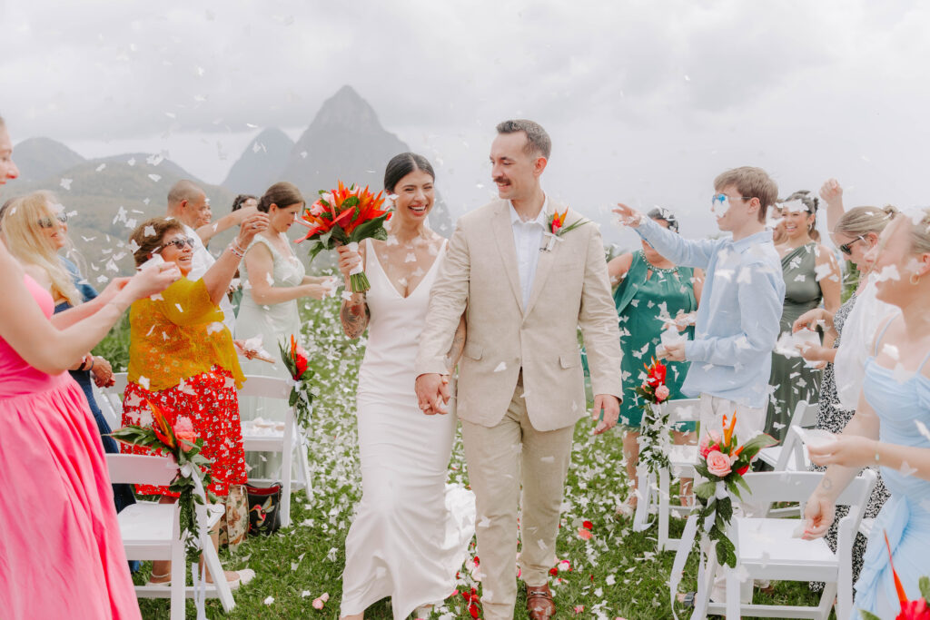 Bride and groom post ceremony with confetti with the Pitons in the background at La Haut Resort in St. Lucia.