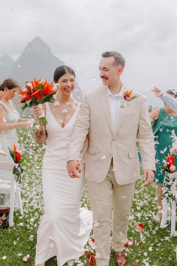 Bride and groom post ceremony with confetti with the Pitons in the background at La Haut Resort in St. Lucia.