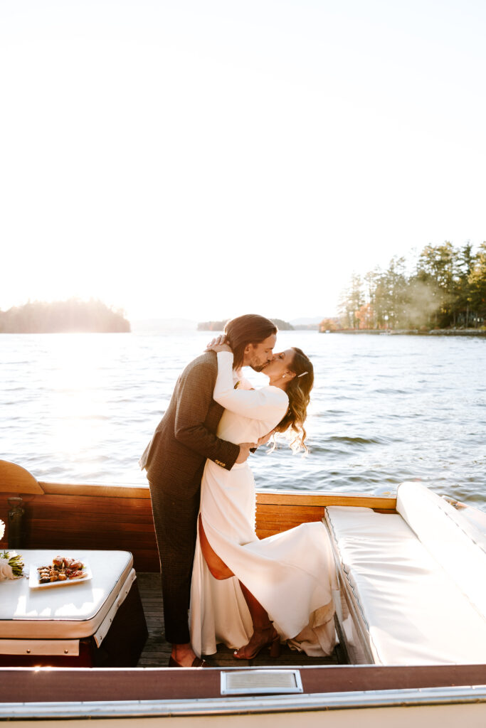 Bride and groom kiss on boat at Migis lodge lawn on Sebago lake, Maine