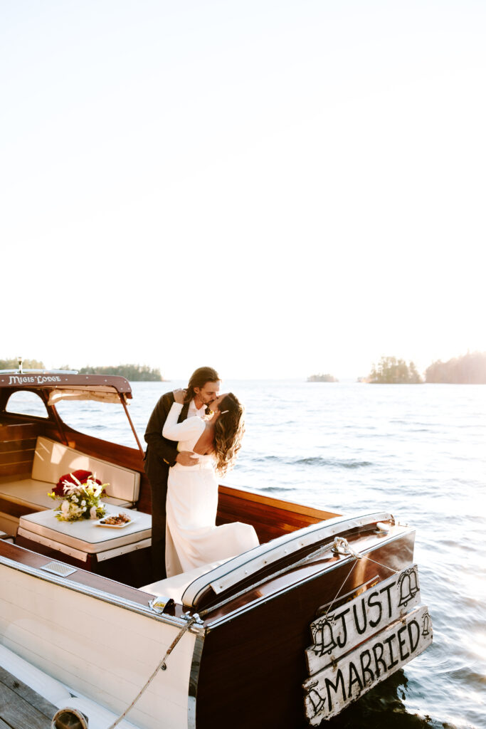 Bride and groom kiss on boat at Migis lodge lawn on Sebago lake, Maine