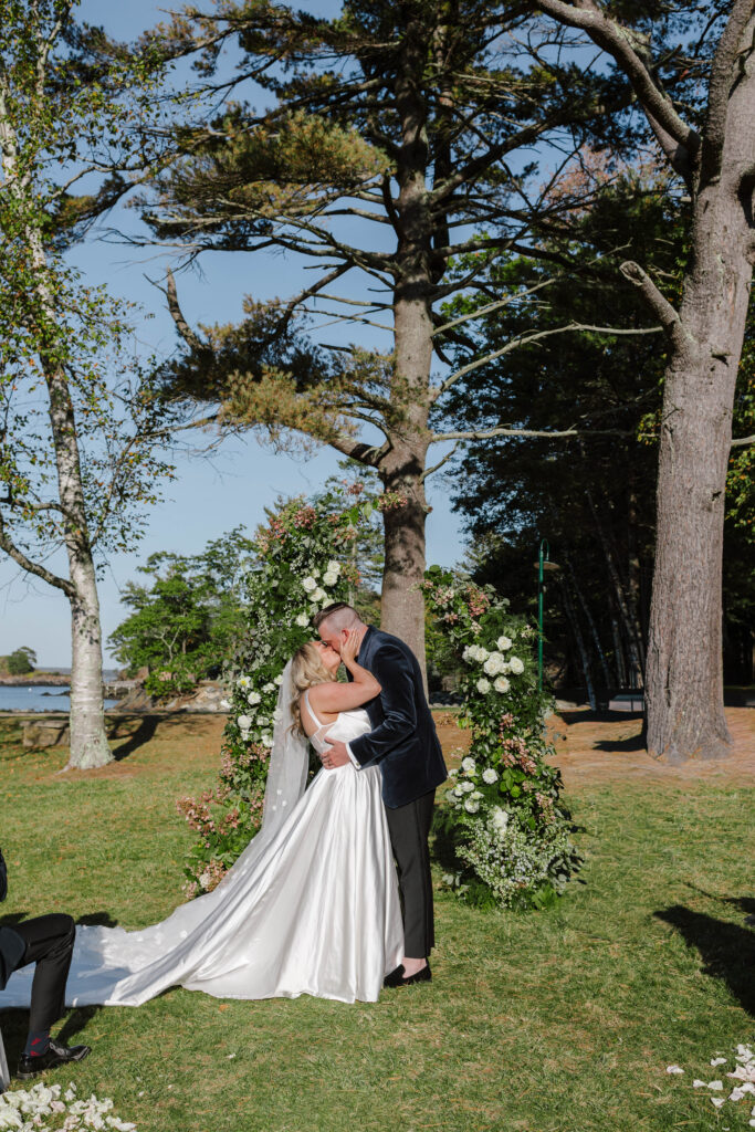 Bride and groom have first kiss under the trees during their Maine island wedding