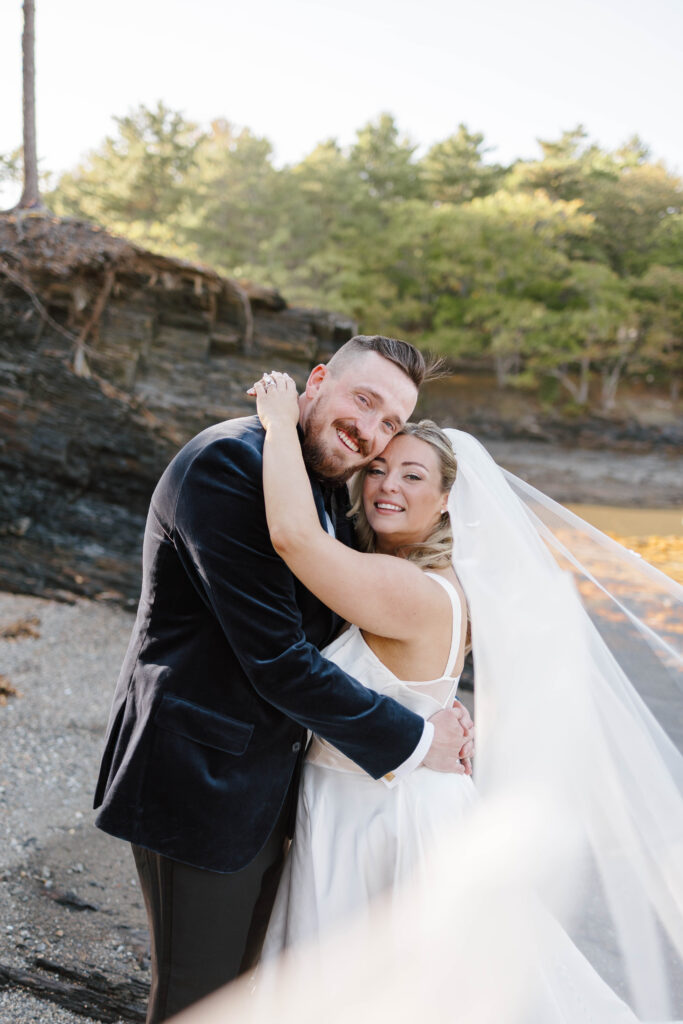 Bride and groom walking hand in hand along the shoreline during their coastal Maine wedding