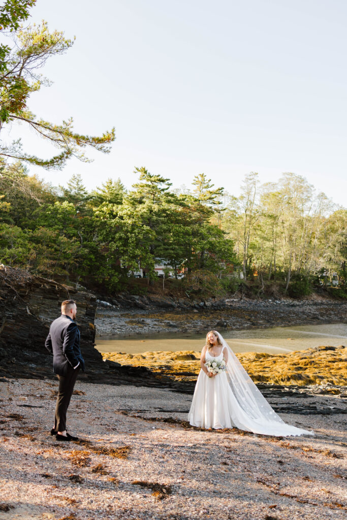 Bride and groom walking hand in hand along the shoreline during their coastal Maine wedding
