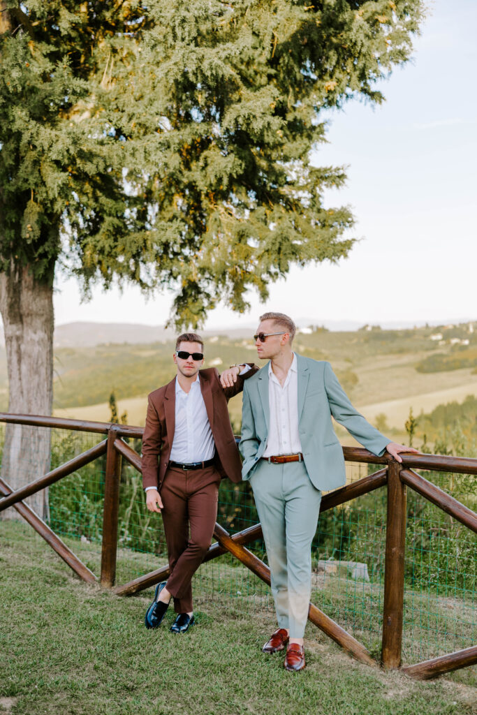 Two grooms pose for camera on welcome party evening the night before their Tuscan wedding