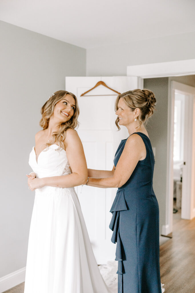 mother of bride helps get bride into dress in boston, massachusetts