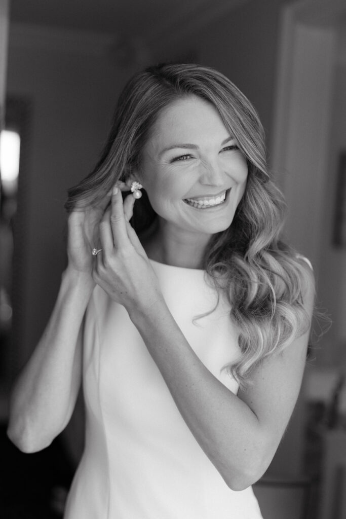 bride smiles at camera as she puts ear rings on taken by boston photographer