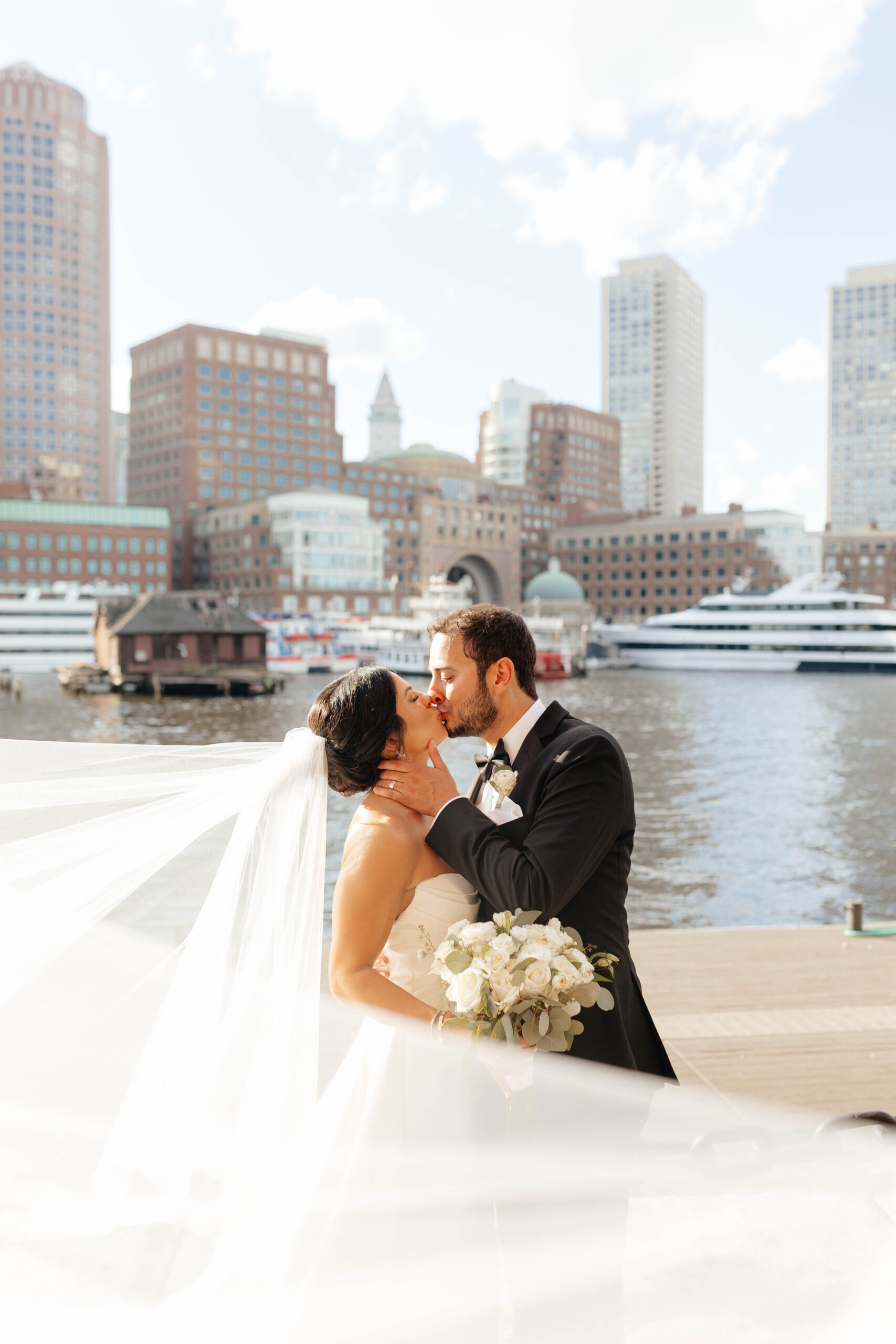 bride and groom share kiss in front of boston harbor hotel with water in background