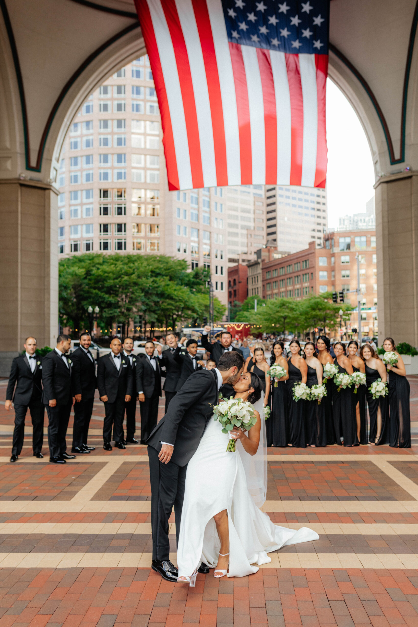 wedding party walking behind bride and groom at boston harbor hotel with american flag in background