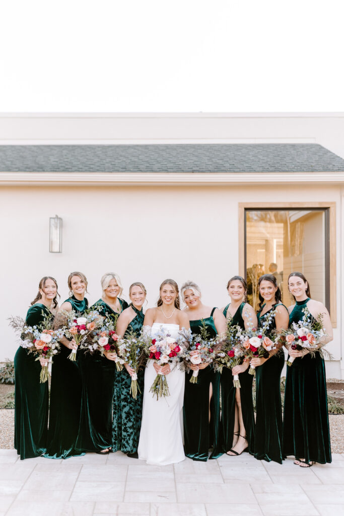 bridesmaids smile with bride holding colorful winter floral bouquets.