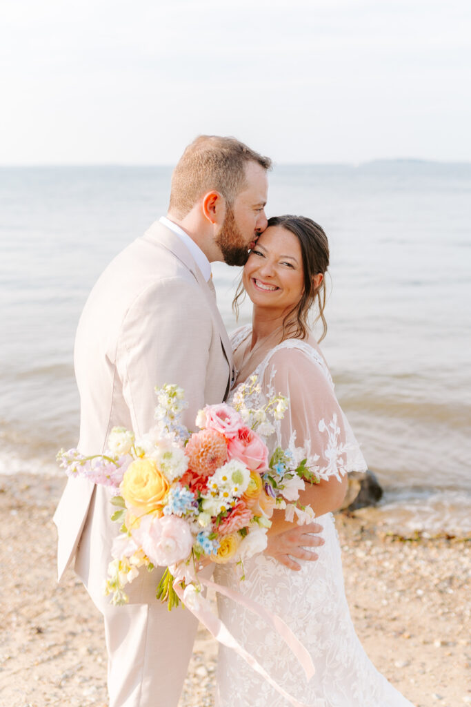 groom kisses bride on cheek on beach in cape cod