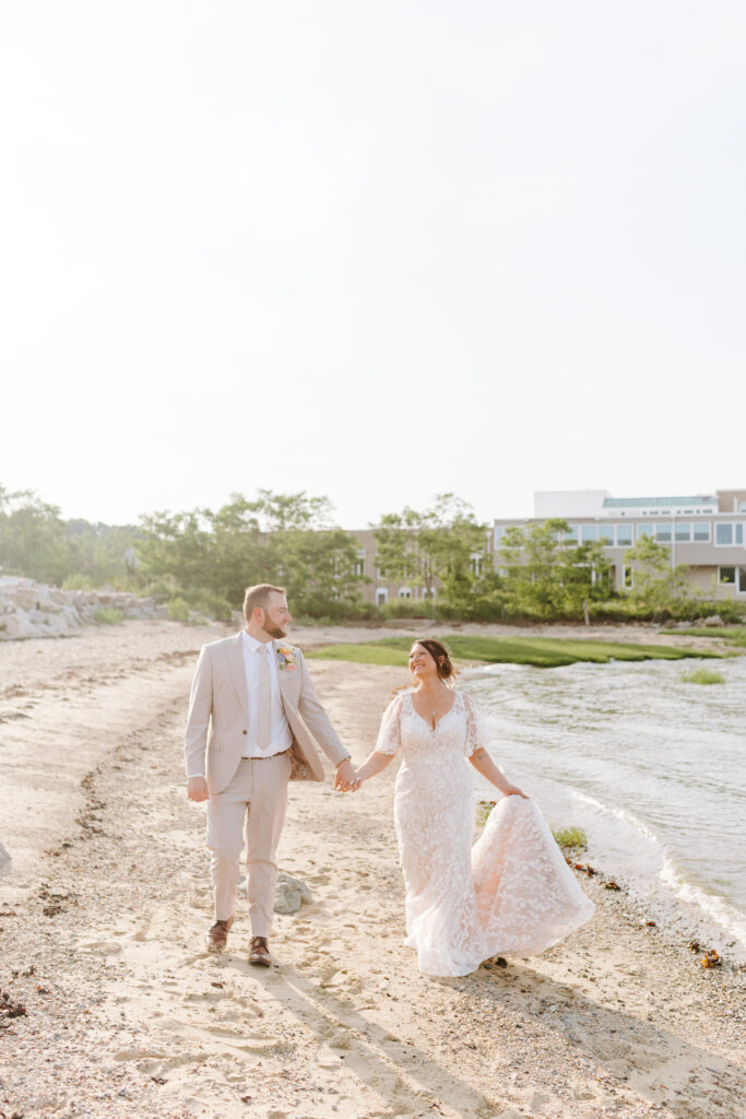 bride and groom hold hands and walk on beach in plymouth massachusetts