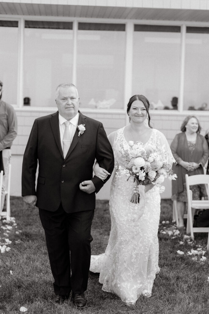 black and white photo of bride walking down with father at wedding ceremony