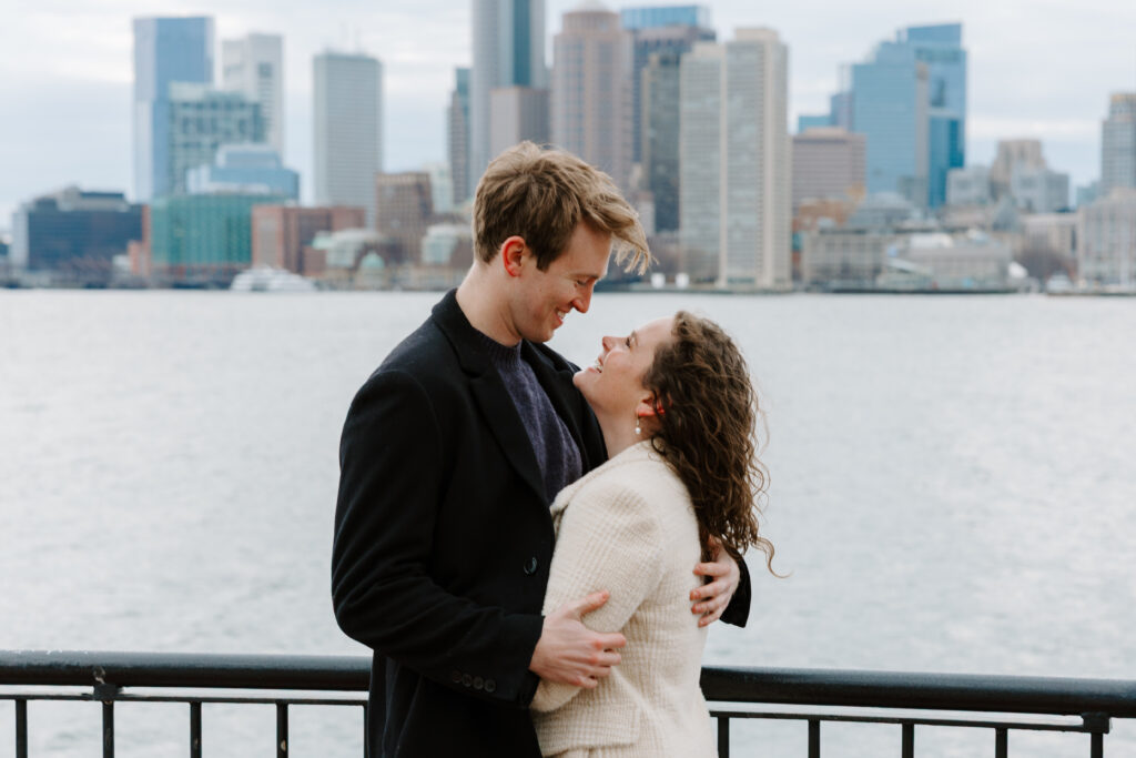 Boston skyline engagement photos with couple embracing on East Boston waterfront