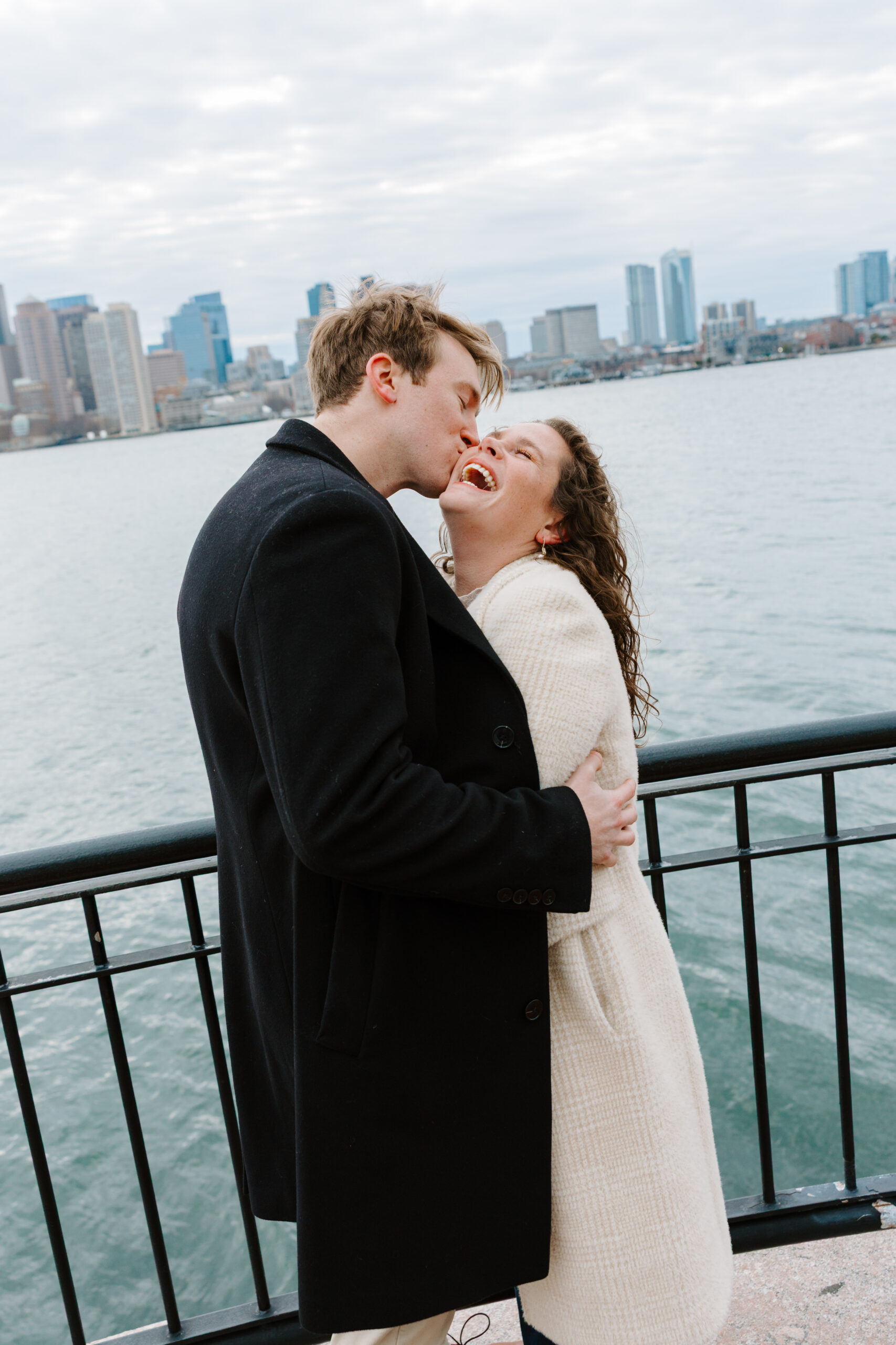 Joyful candid engagement moment with Boston skyline and waterfront backdrop