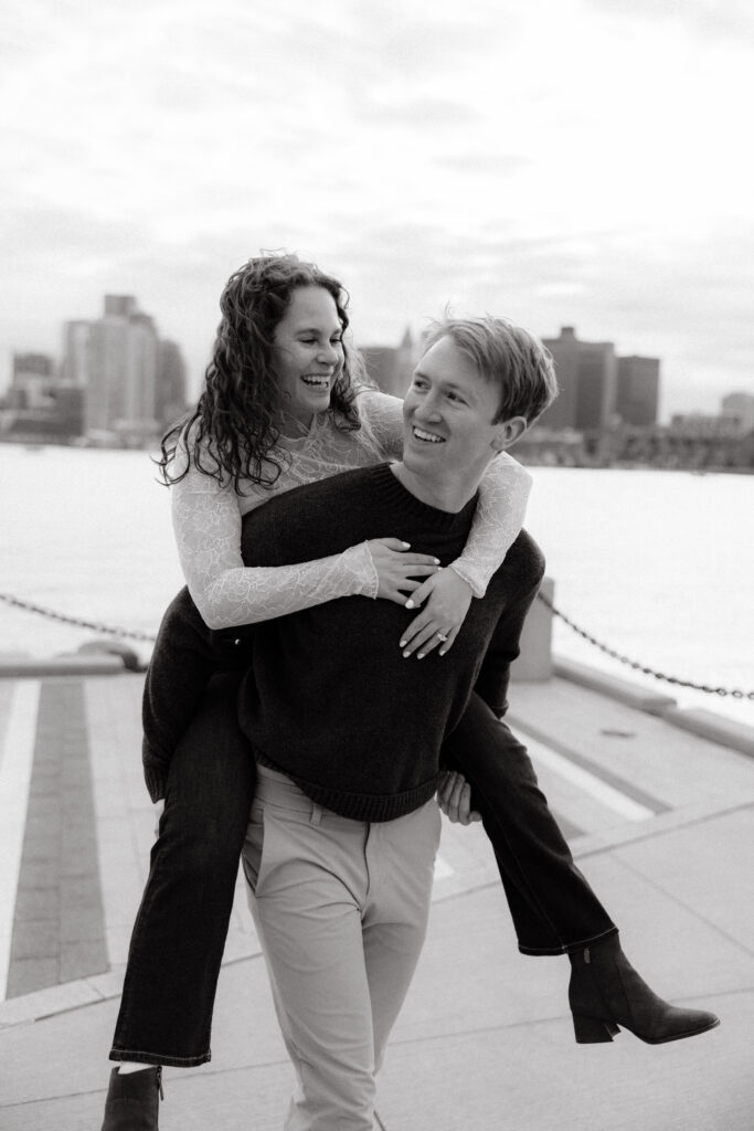 Playful piggyback engagement photo with Boston skyline in East Boston