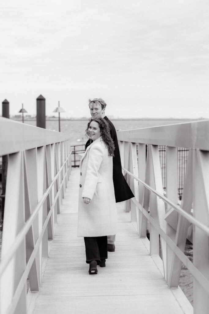 Black and white engagement photo of couple walking on pier in East Boston waterfront