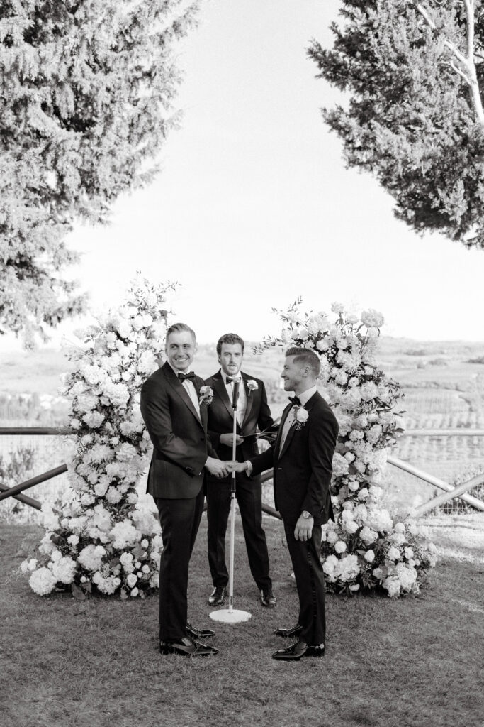 grooms hold hands at wedding ceremony in tuscany, italy