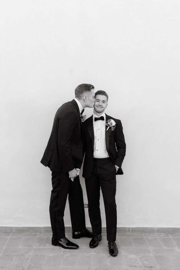 groom kisses groom on cheek in black and white photo at wedding