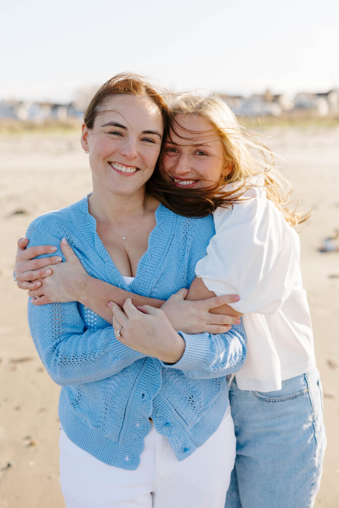 Two women cuddling in beach grass dunes in Boston engagement photos