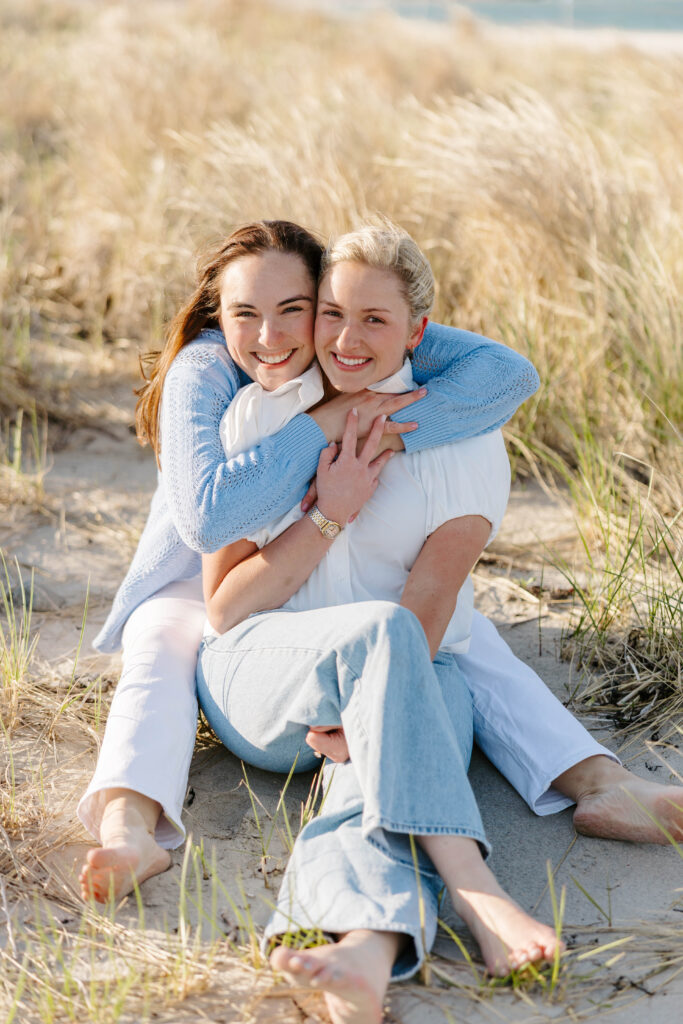 Two women smiling at each other during windy Boston beach engagement session