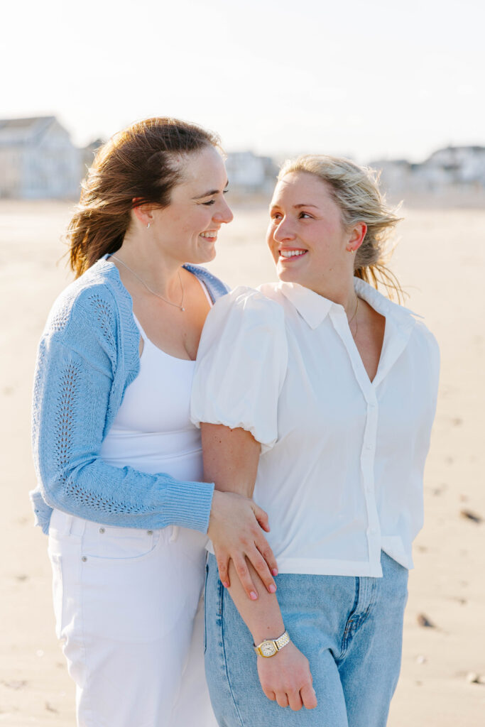 Two women hugging and smiling on East Boston beach during engagement session