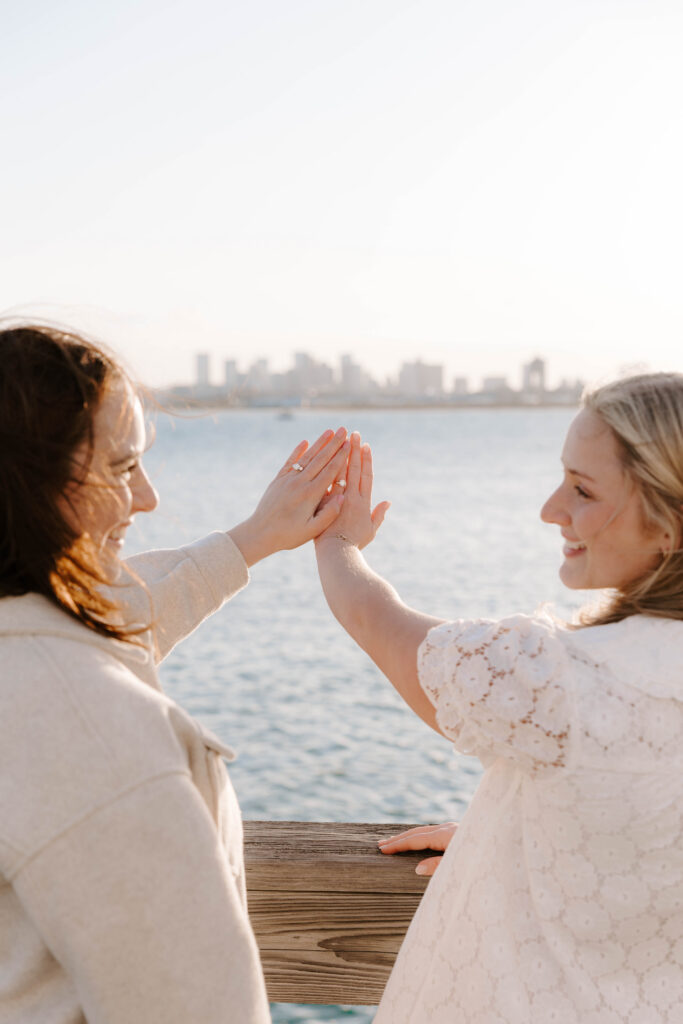 Couple showing engagement rings near Boston harbor