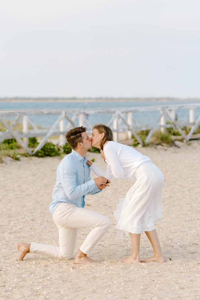 man and woman kiss while he is on one knee proposing