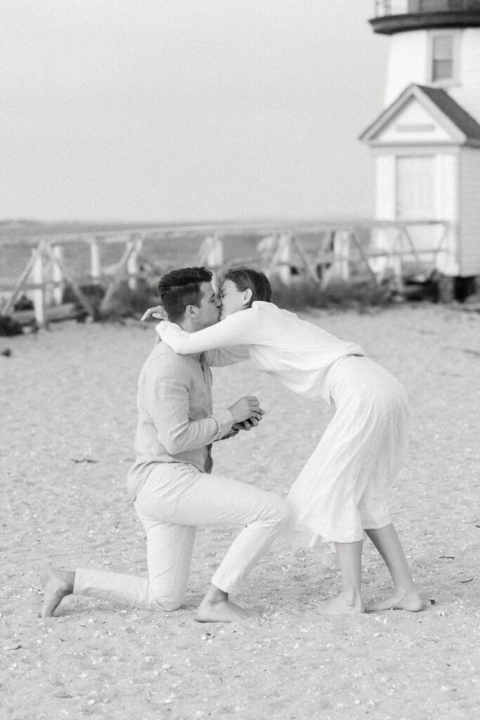 woman kisses man as he proposes on beach in nantucket, massachusetts