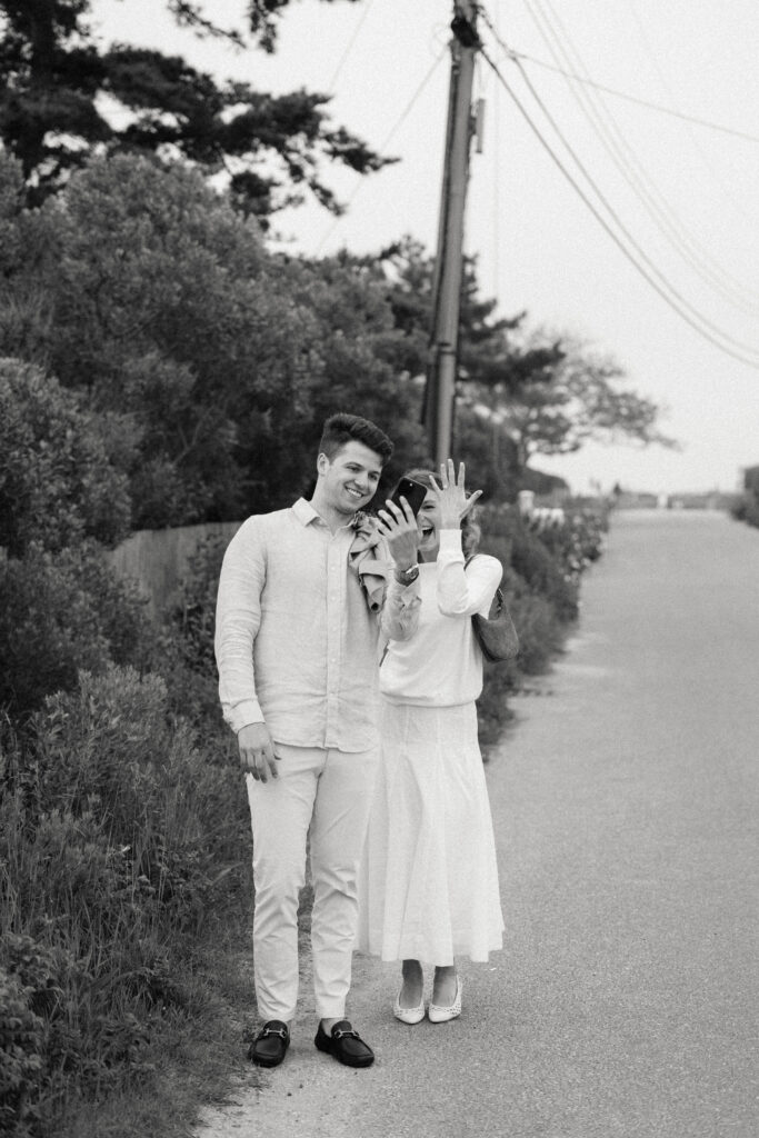 black and white photo of woman holding hand up in the air to celebrate engagement to friends on facetime