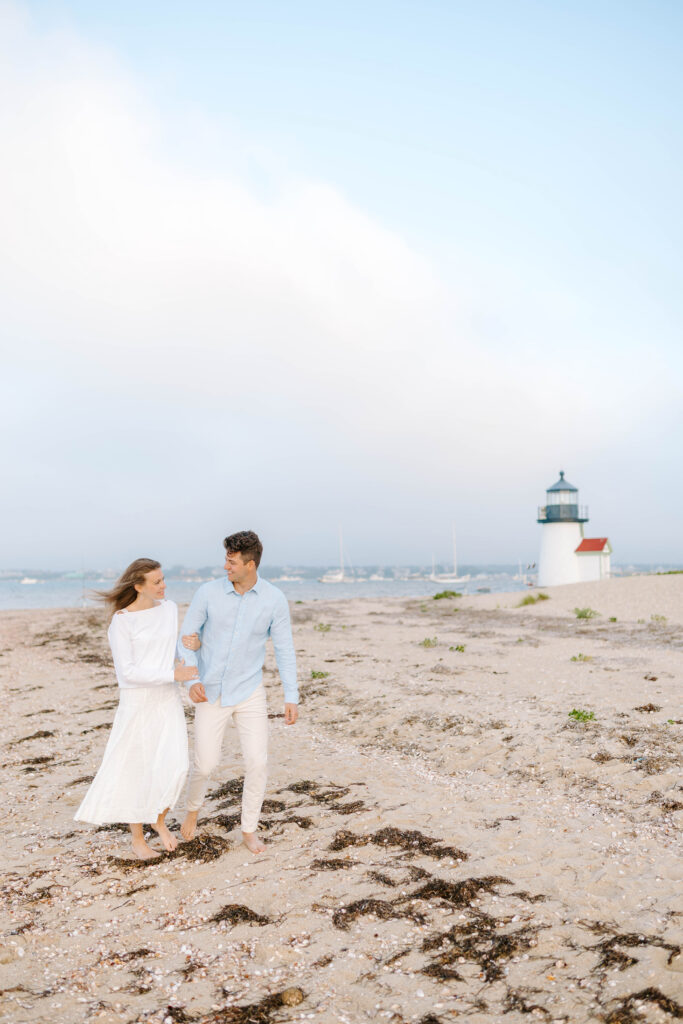 woman and man walk on beach with lighthouse in the background taken by talented wedding photographer