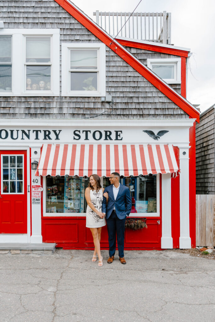Red and white storefront engagement photo in Rockport Massachusetts