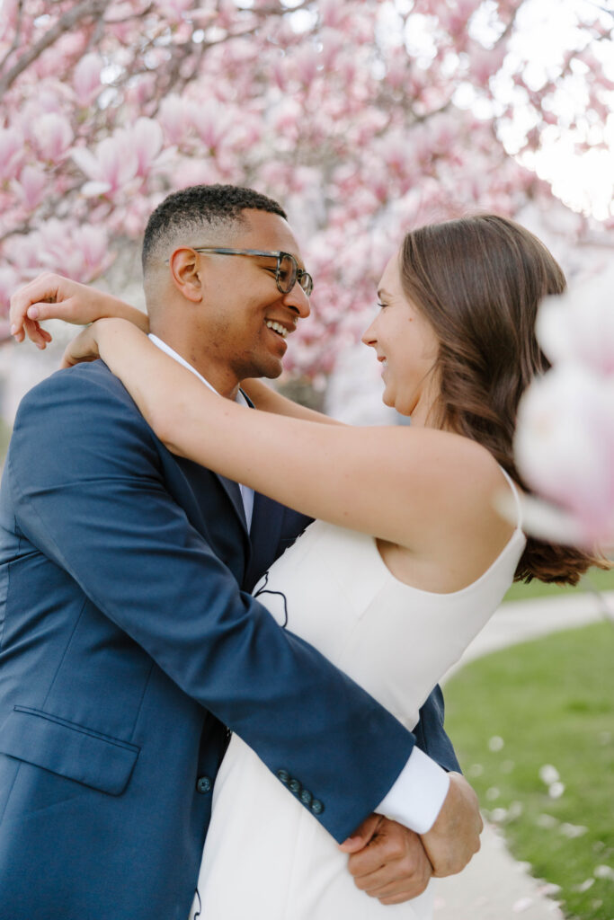 Close up of couple smiling under pink blossoms during engagement session