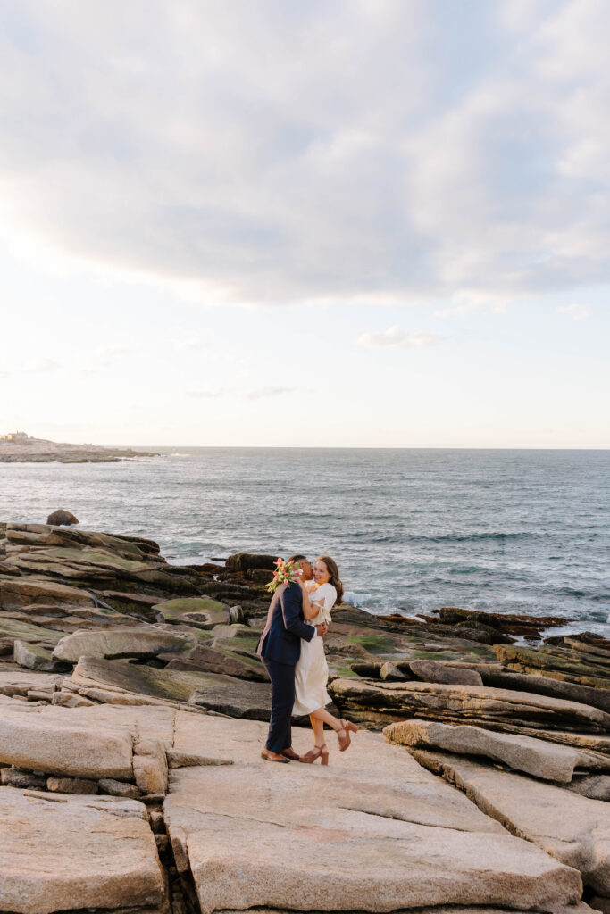 Couple embracing on rocky coastline at sunset in Rockport Massachusetts
