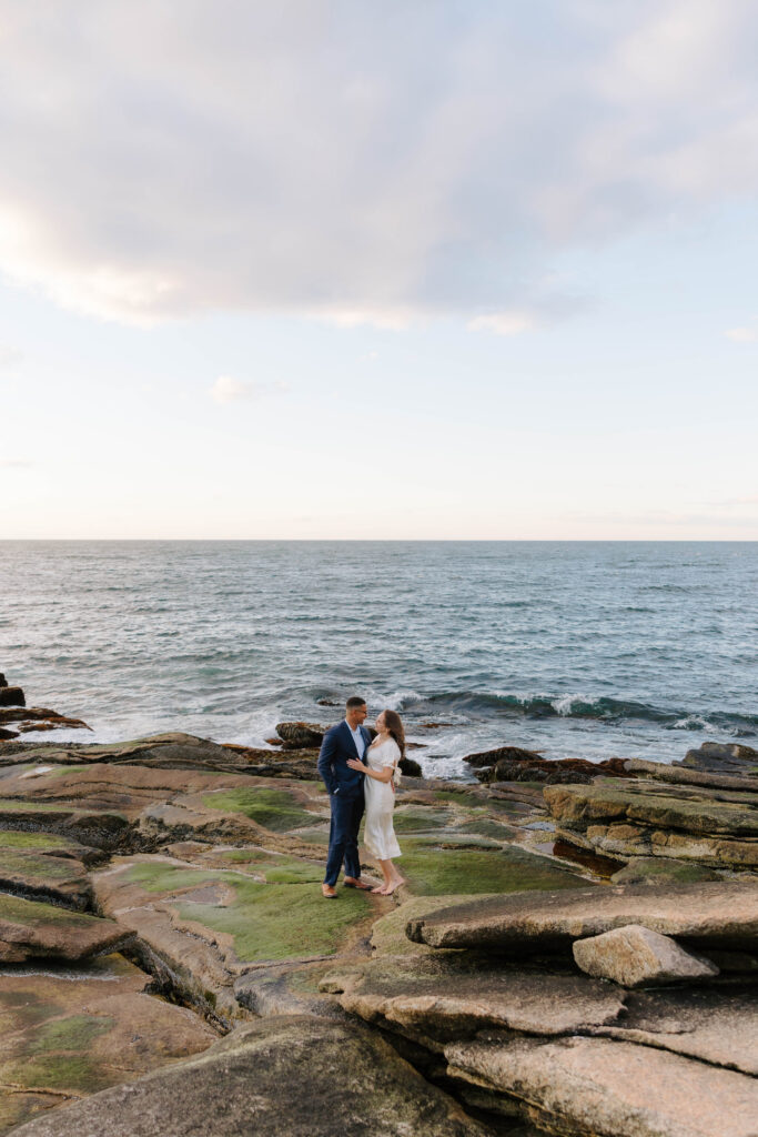 Wide shot of couple standing on rocky shoreline with ocean view