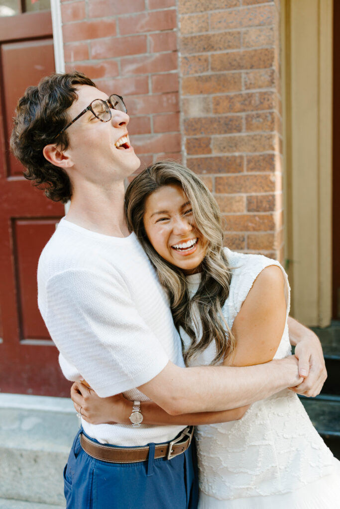 Margaret and Chris laughing together during their Beacon Hill Boston engagement session beside historic brick buildings