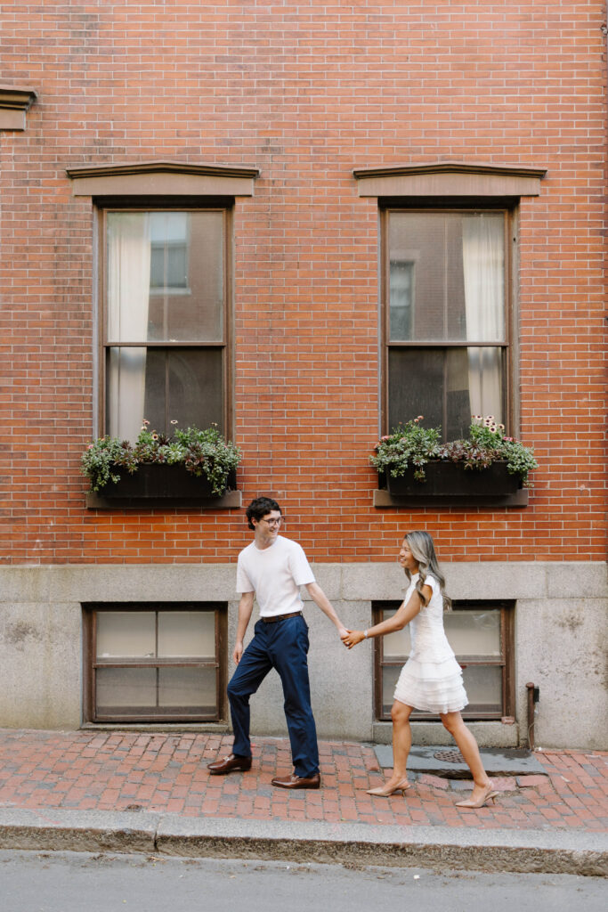 Margaret and Chris walking together on a cobblestone street during their Beacon Hill engagement session