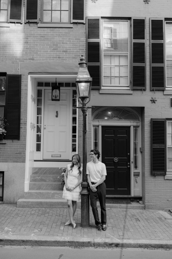 Black and white engagement portrait of Margaret and Chris standing beside a historic Beacon Hill street lamp