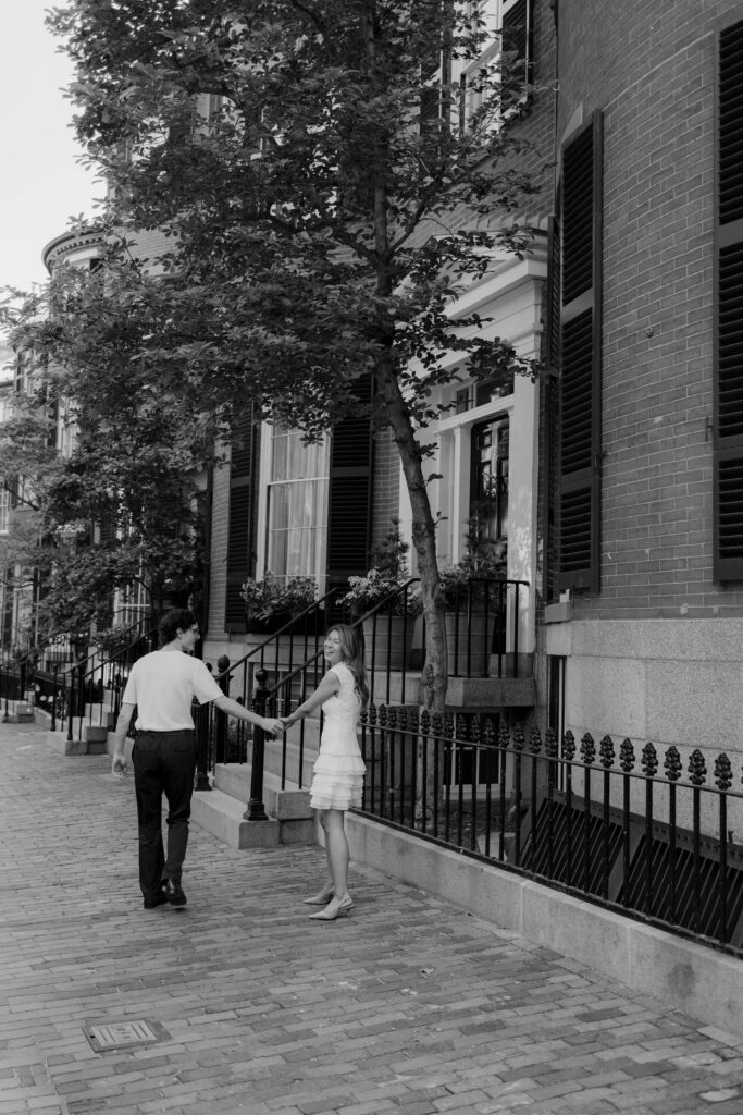 Black and white engagement photo of couple walking through Beacon Hill Boston holding hands