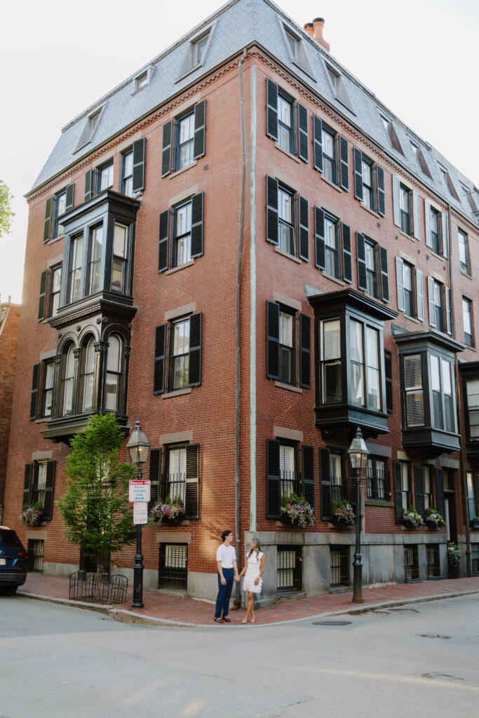 Wide angle engagement photo of man and woman standing beside historic Beacon Hill brownstones