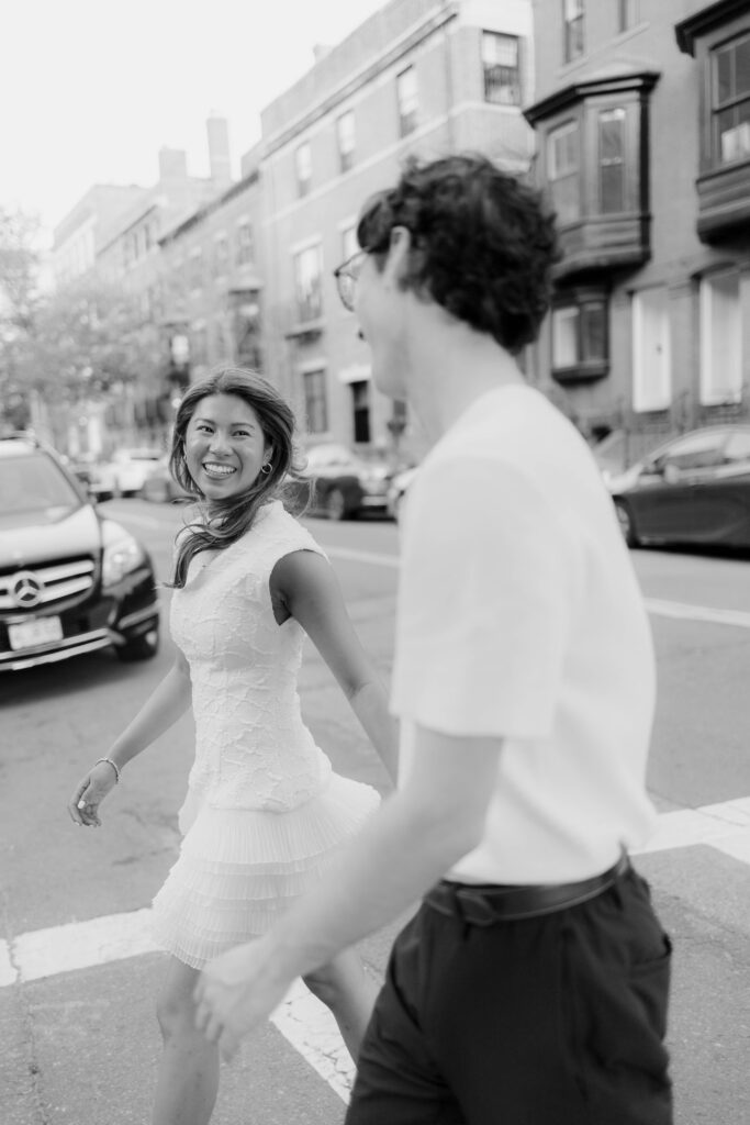 Black and white candid engagement photo of man and woman walking through Boston