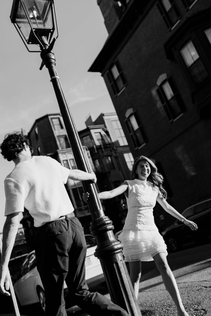 Artistic black and white engagement photo of couple spinning around a Beacon Hill street lamp