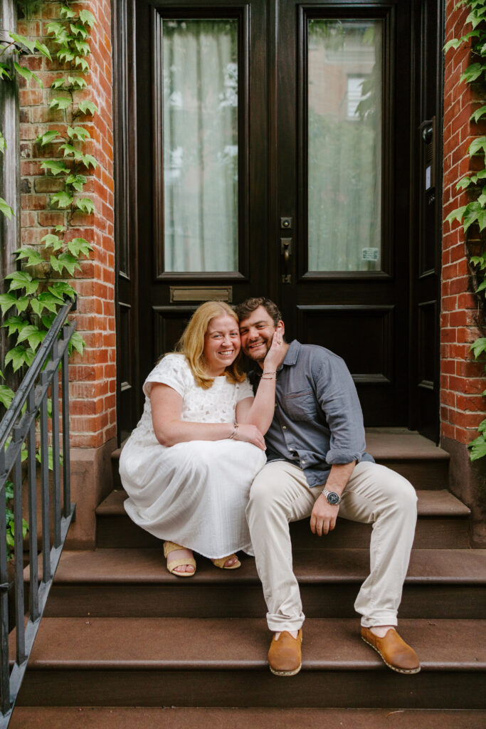 Couple sitting on brownstone steps during cozy West Village NYC engagement session. Photo by Clay Taylor Photo