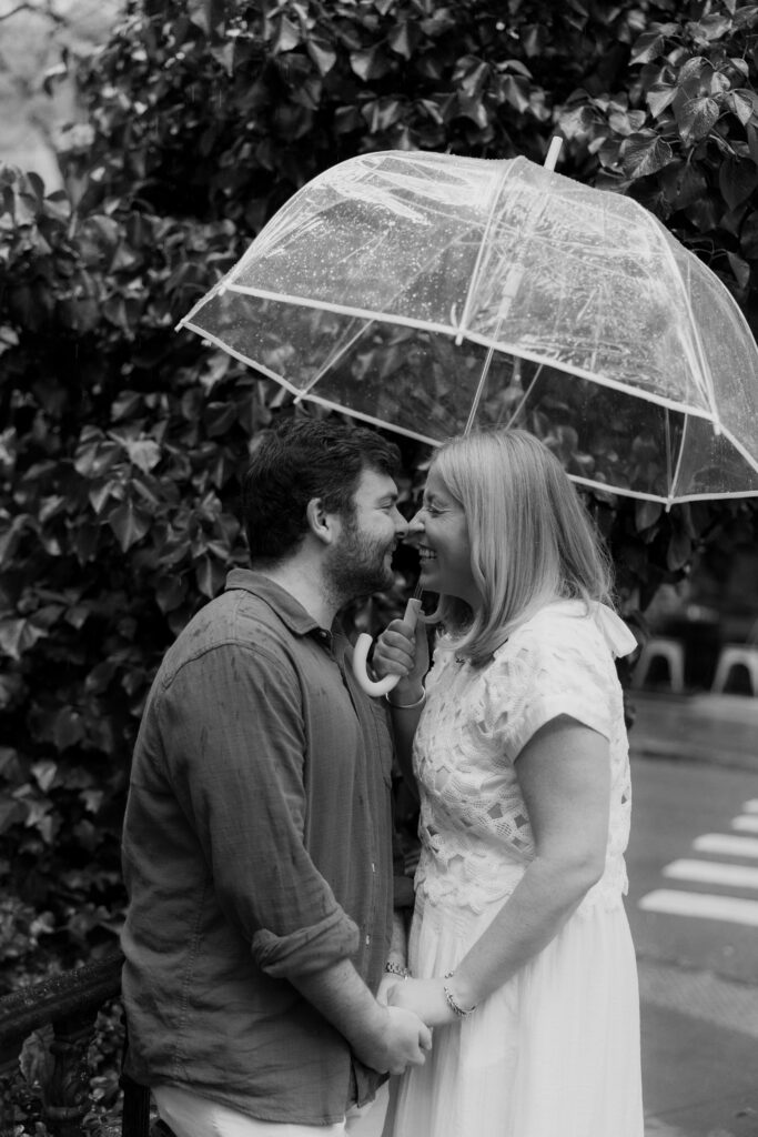 Couple laughing under a clear umbrella during rainy West Village NYC engagement session. Photo by Clay Taylor Photo
