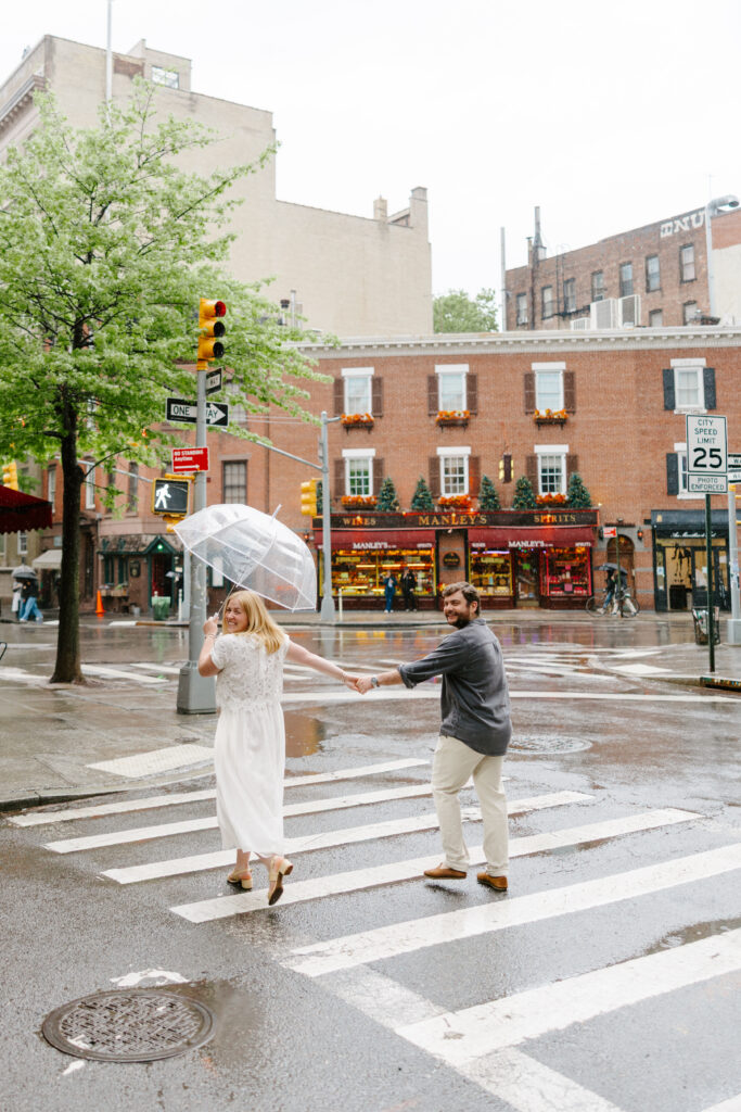 Couple crossing the street in the rain during New York City West Village engagement session. Photo by Clay Taylor Photo