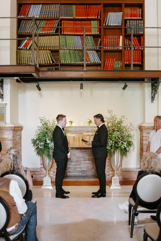 Wide ceremony photo of Ryan and Spencer exchanging vows inside the Boston Public Library wedding space.