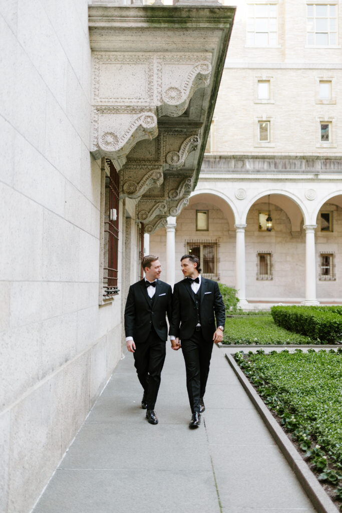 Ryan and Spencer walking hand in hand through the courtyard at the Boston Public Library wedding venue.