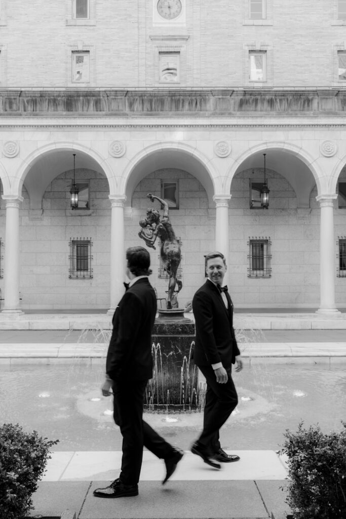 Black and white candid portrait of Ryan and Spencer walking past the fountain courtyard at the Boston Public Library.