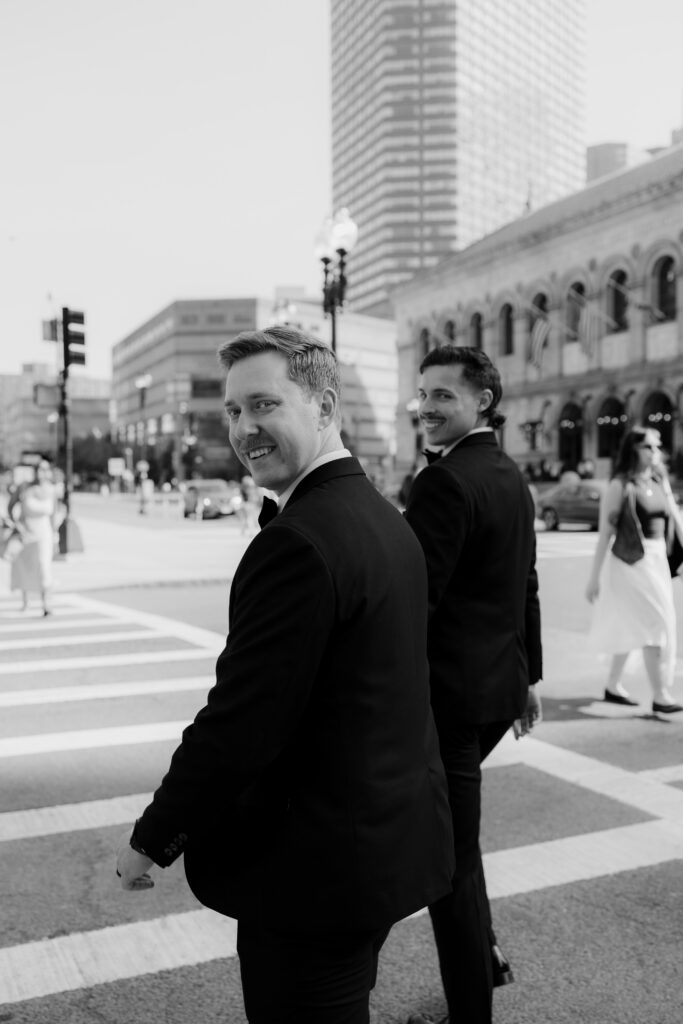 Black and white candid photo of Ryan and Spencer walking through Boston and smiling back at the camera.