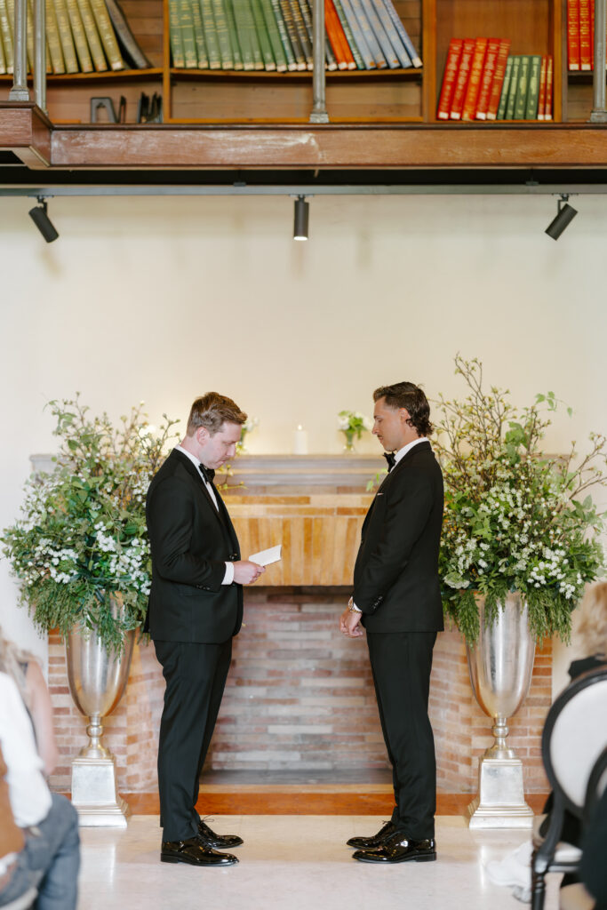 Ryan reading personal vows during his Boston Public Library wedding ceremony surrounded by floral arrangements.
