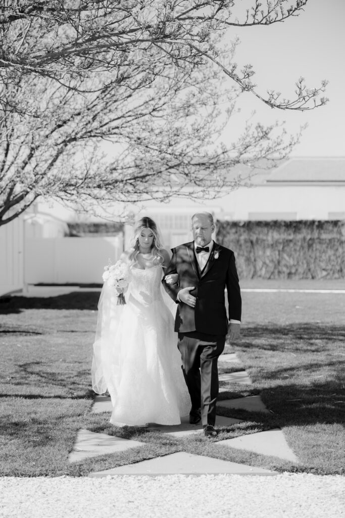 Black and white photo of bride and her father walking down the aisle at ceremony